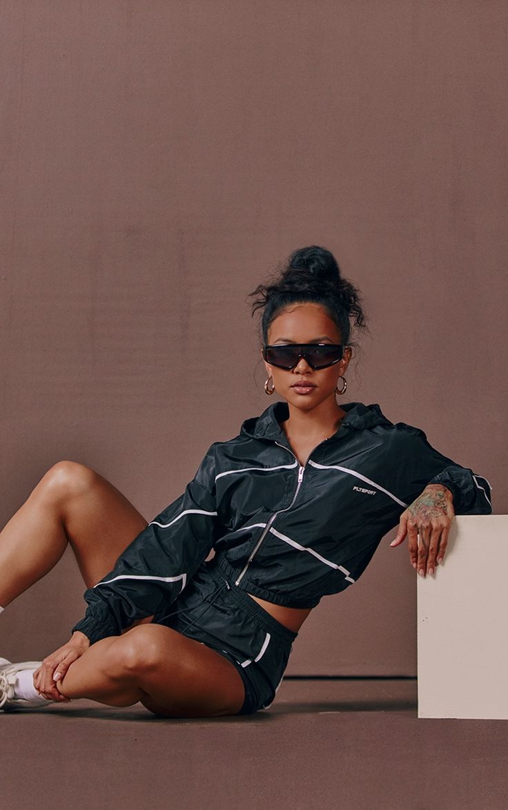 a woman sitting on the ground with her legs crossed, wearing sunglasses and a black jacket