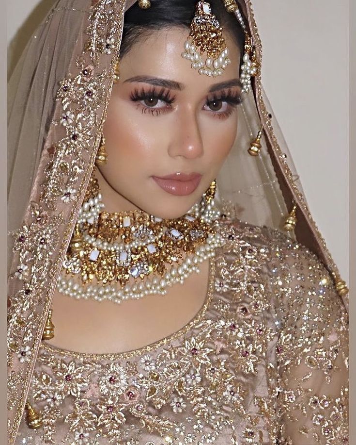 a woman in a bridal gown and veil with pearls on her head, wearing gold jewelry