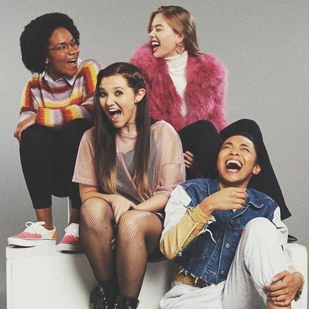 three women and one man sitting on top of a white box with their mouths open