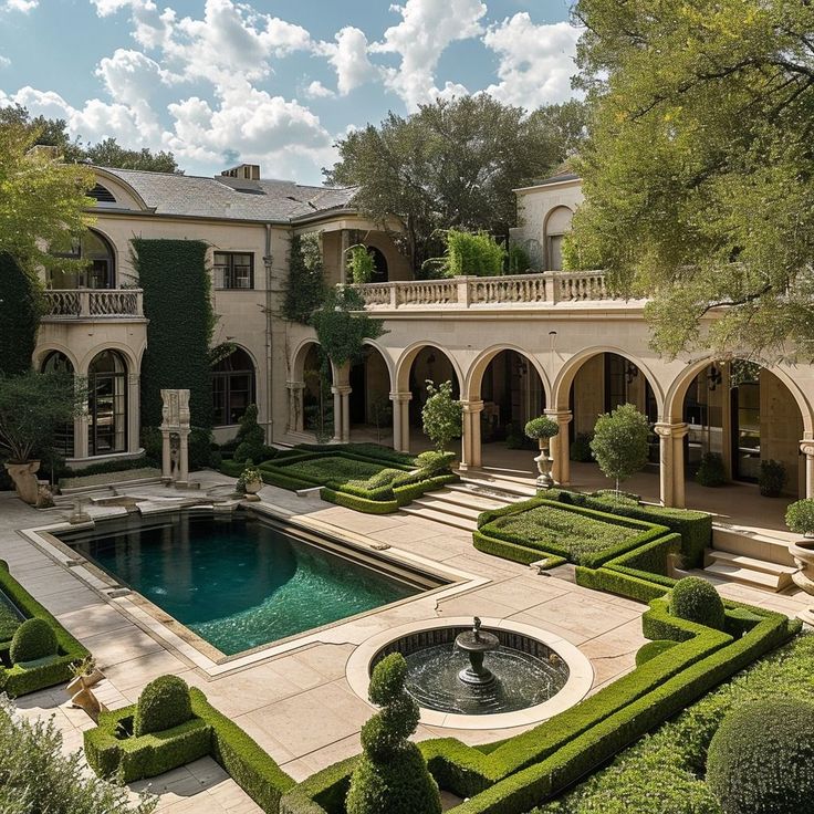 an outdoor pool surrounded by greenery and hedges in front of a large house with a fountain