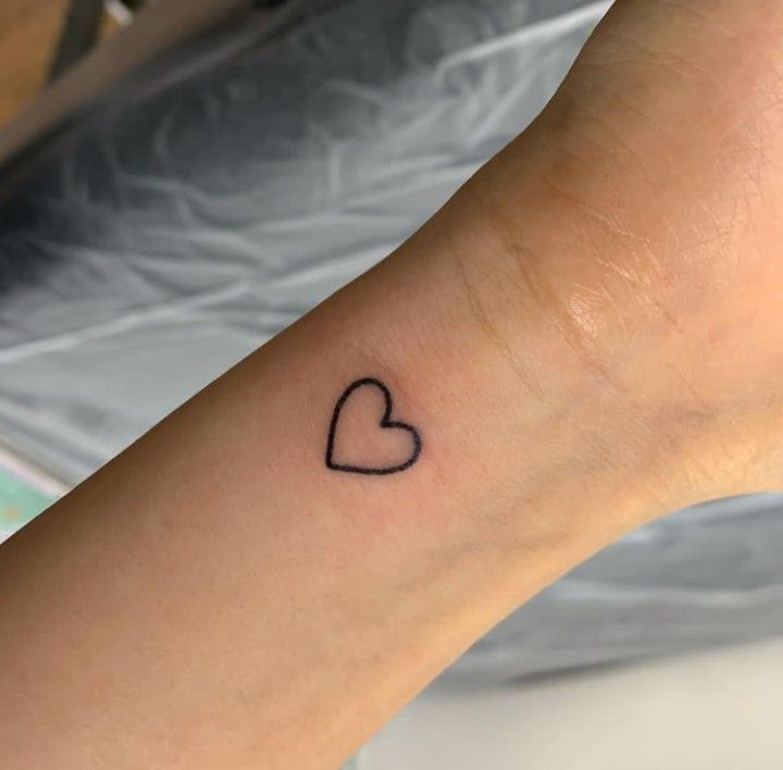 a small heart tattoo on the wrist is shown in black ink with a tiny outline