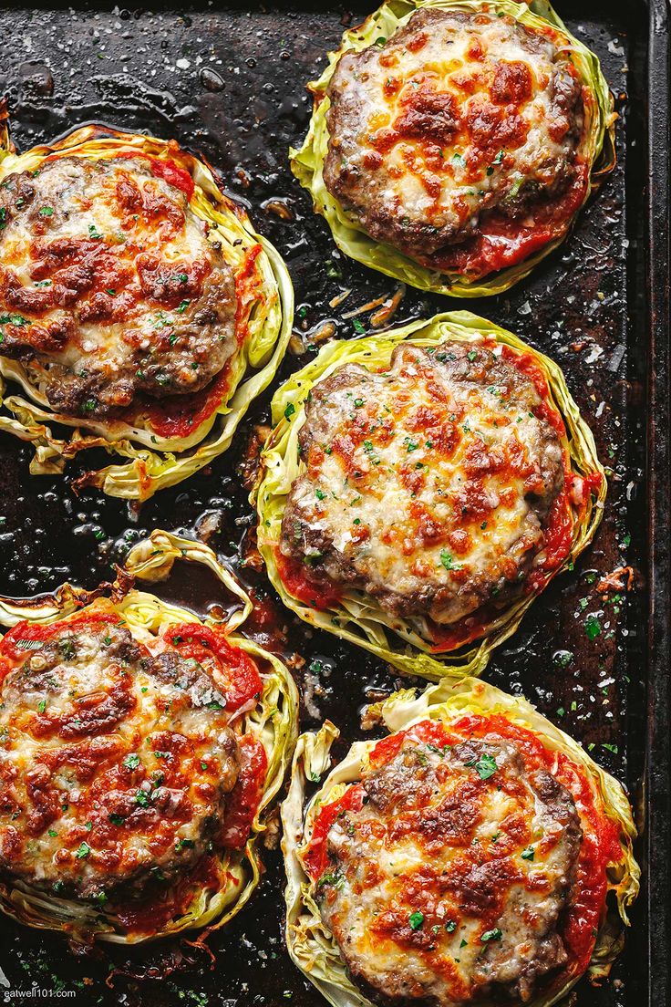 four spaghetti dishes on a baking sheet ready to go in the oven, with cheese and sauce