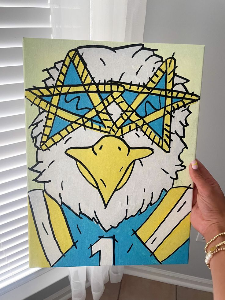 a hand holding up a painting of an eagle with glasses on it's face