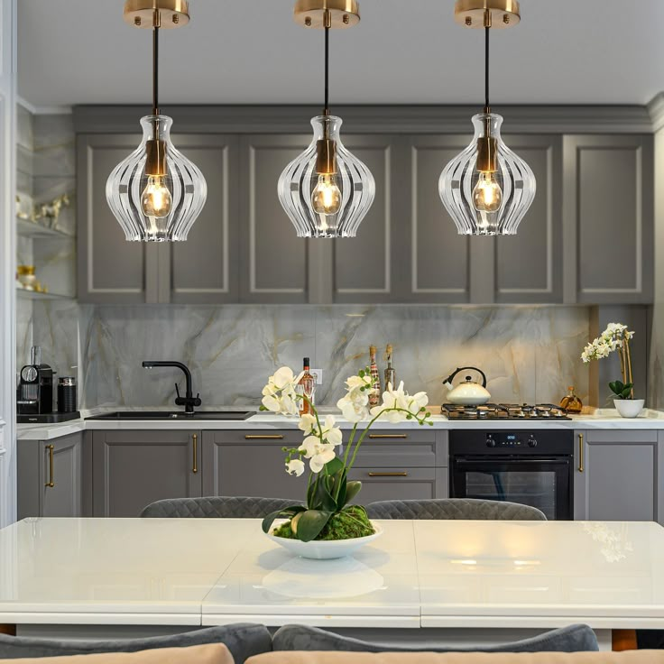 a kitchen with grey cabinets and white counter tops, lights hanging from the ceiling over an island