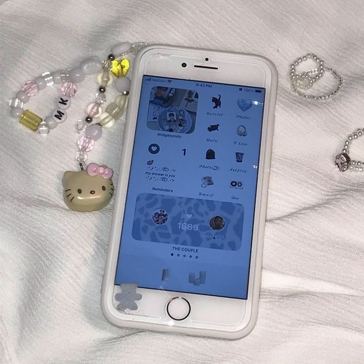 an iphone is laying on a bed next to some beads and necklaces, with a hello kitty keychain