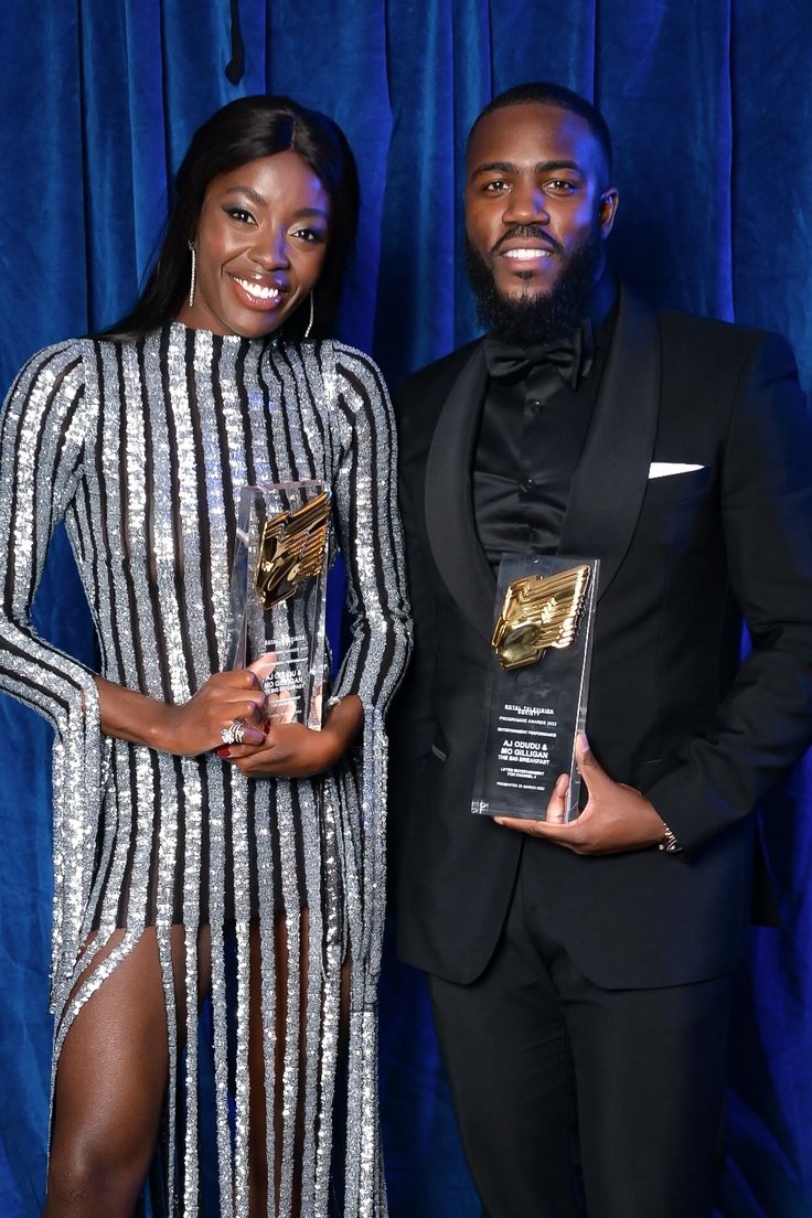 a man and woman standing next to each other in front of a blue curtain holding awards