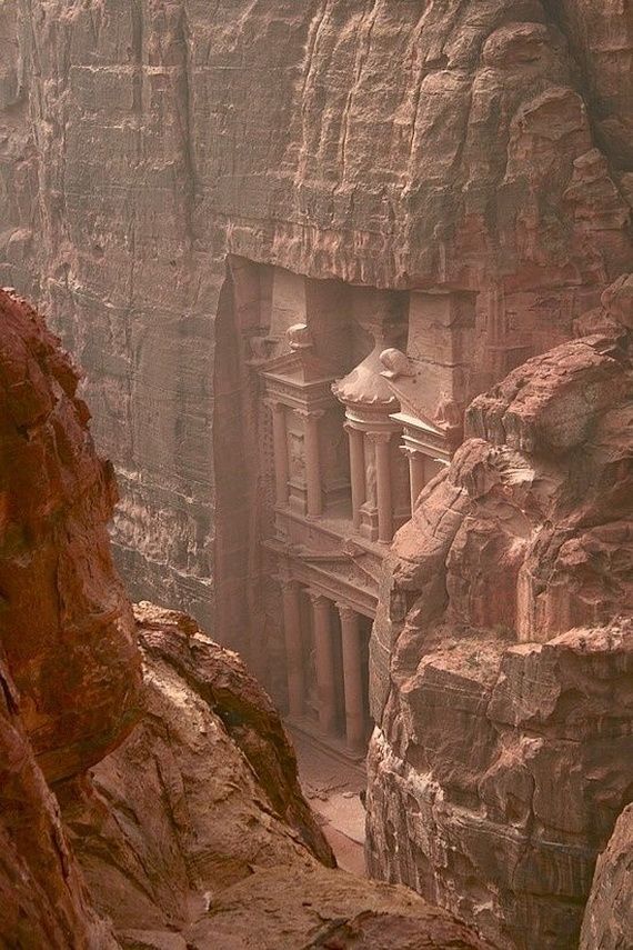 a man standing on top of a cliff next to a building in the middle of a canyon