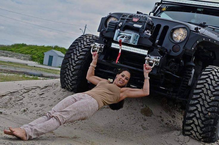 a woman laying on the ground next to a jeep with her hands in the air