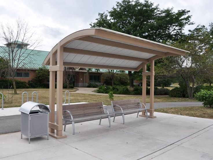 two benches and a trash can in front of a building with a covered area on the sidewalk