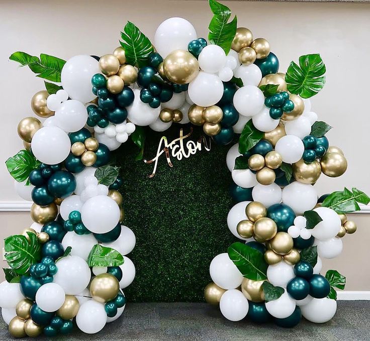 the balloon arch is decorated with green and white balloons, greenery, and leaves