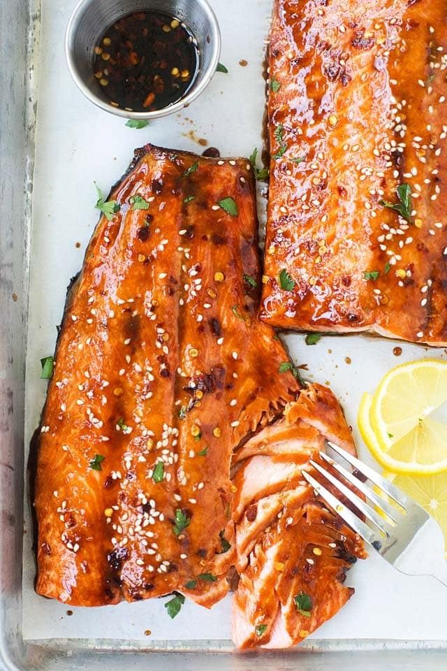 two salmons on a tray with sauce and lemon wedges next to each other