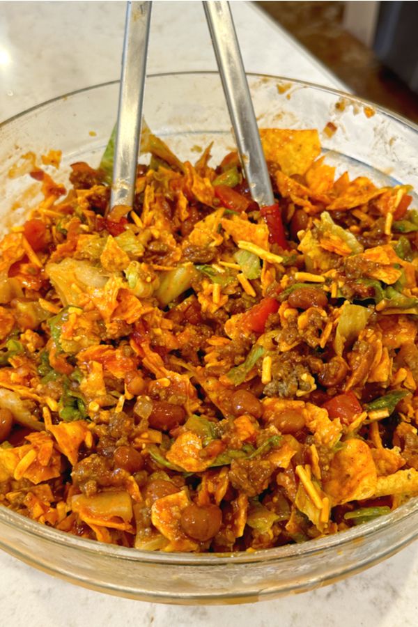 a glass bowl filled with food on top of a white counter next to a pair of tongs