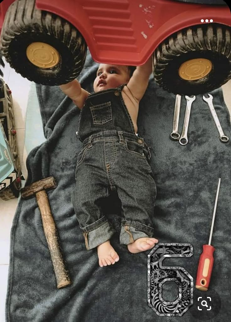 a baby laying on top of a giant red monster truck with lots of tools around it