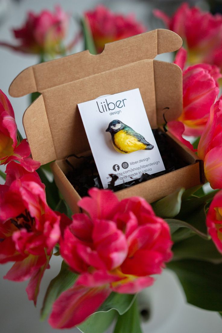 a small yellow and black bird sitting in a cardboard box on top of red flowers