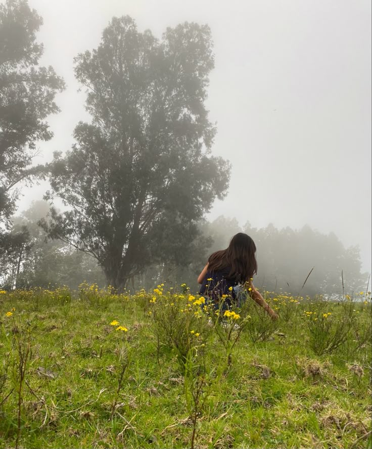 a woman kneeling down in the middle of a field with yellow flowers and trees behind her