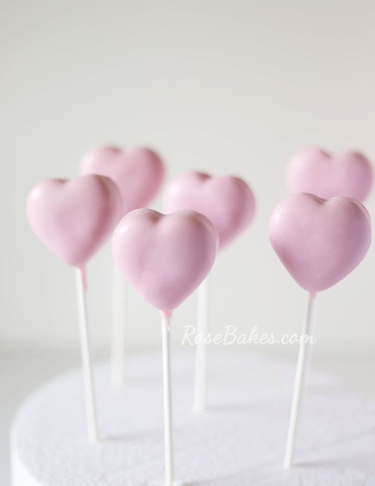 pink heart shaped lollipops sitting on top of a white cake