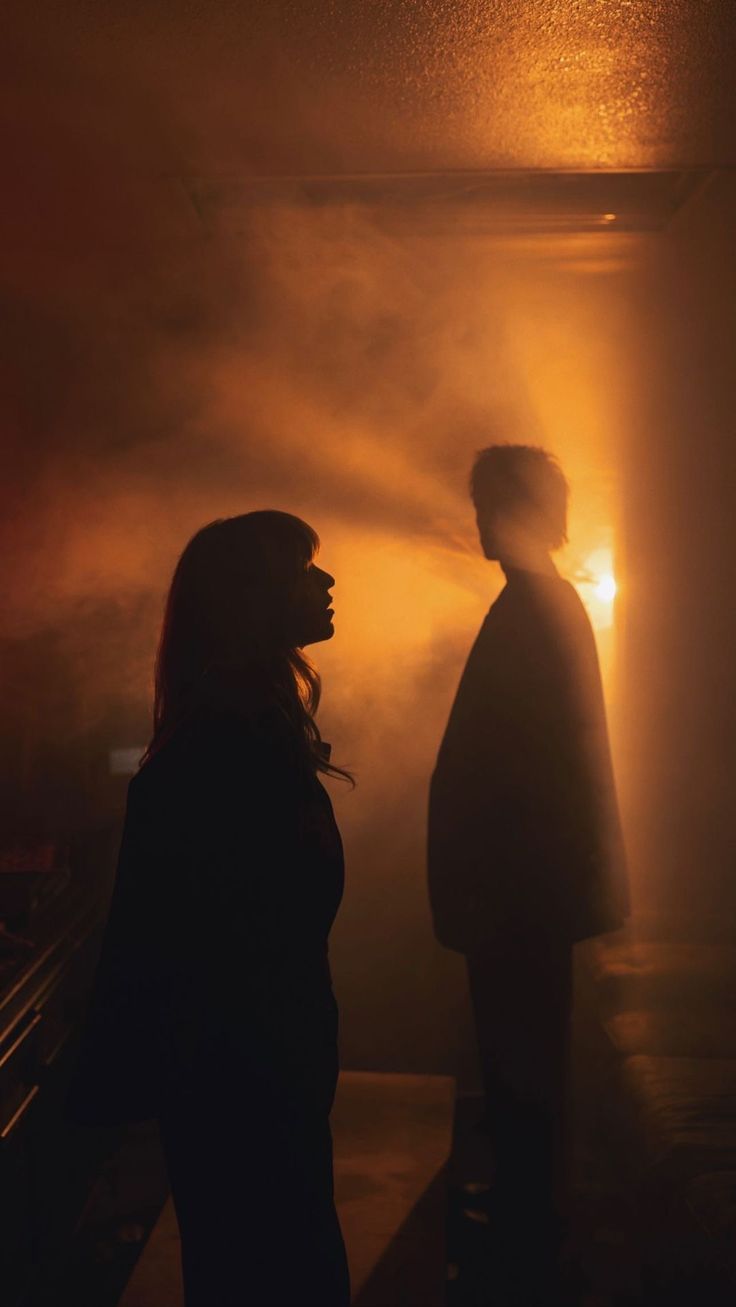 two people standing next to each other in front of a light that is shining on them