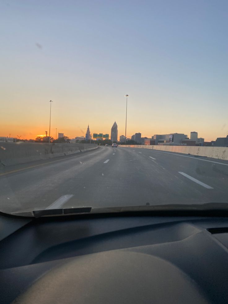 the sun is setting on an empty highway with water and buildings in the back ground