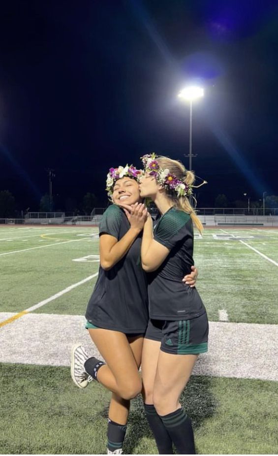 two female soccer players hugging each other on the field at night with lights in the background