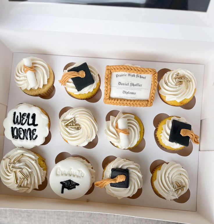 cupcakes with white frosting and black icing are in a box on the table