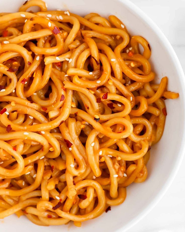 a white bowl filled with noodles covered in cheese and chili sauce on top of a marble table