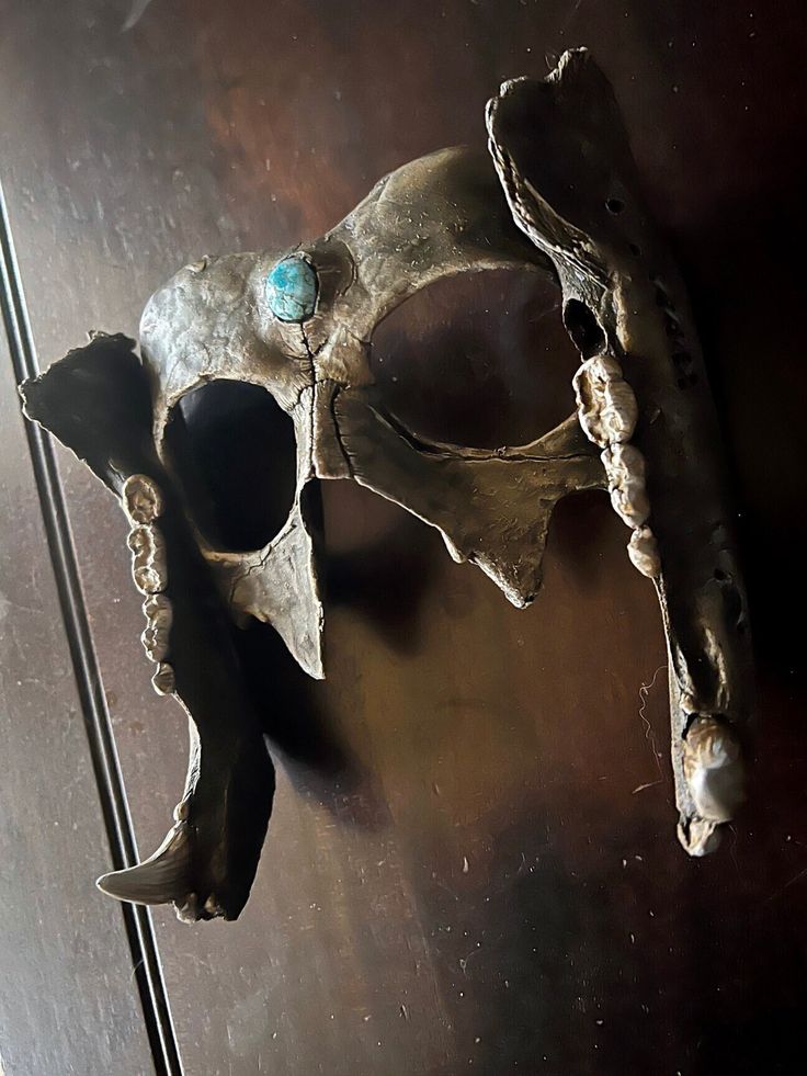 a metal mask hanging on the side of a wooden wall next to a door with glass knobs