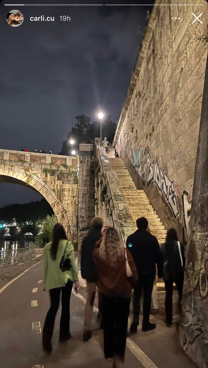 people are walking up and down the stairs in front of an old stone bridge with graffiti on it