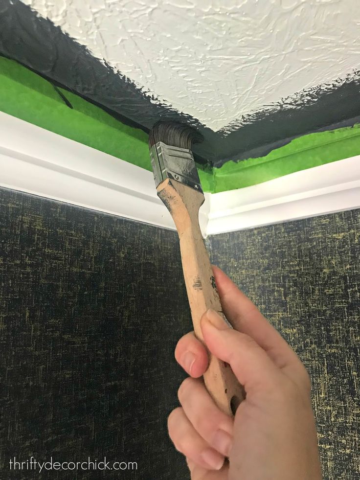 a person holding a paintbrush in their right hand and painting the ceiling with green tape