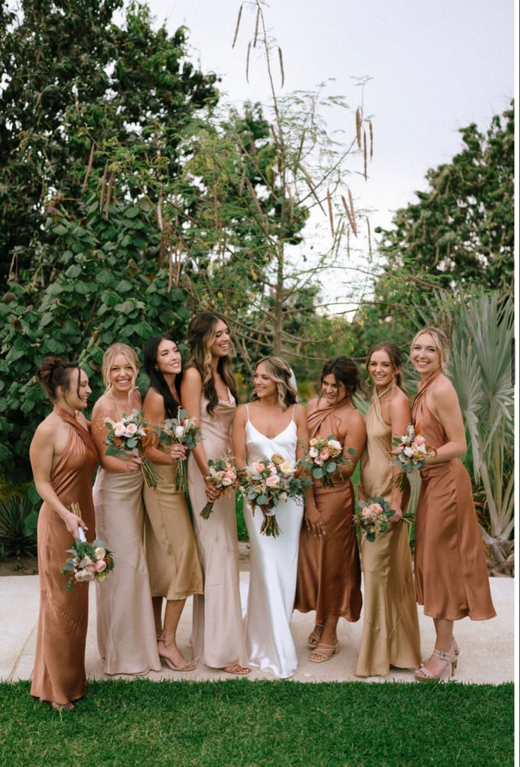 a group of women standing next to each other in front of some bushes and trees