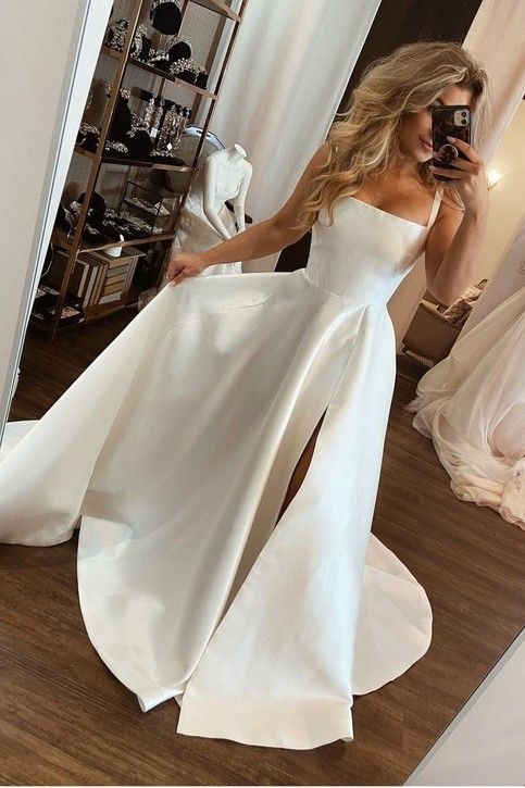 a woman taking a selfie while wearing a white wedding dress with high slits