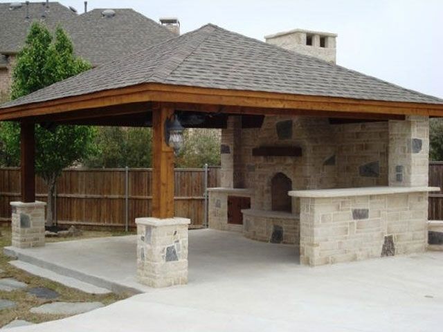 an outdoor bbq and grill area in a backyard with stone pillars, brick walls and a wooden roof