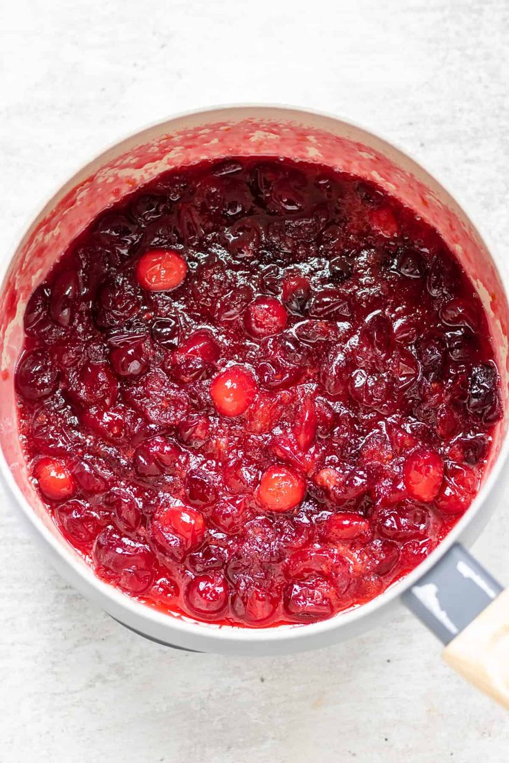 a pot filled with cranberry sauce on top of a white counter next to a spatula