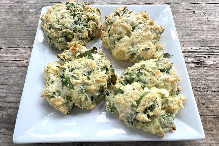 four biscuits with spinach and cheese are on a white plate, ready to be eaten