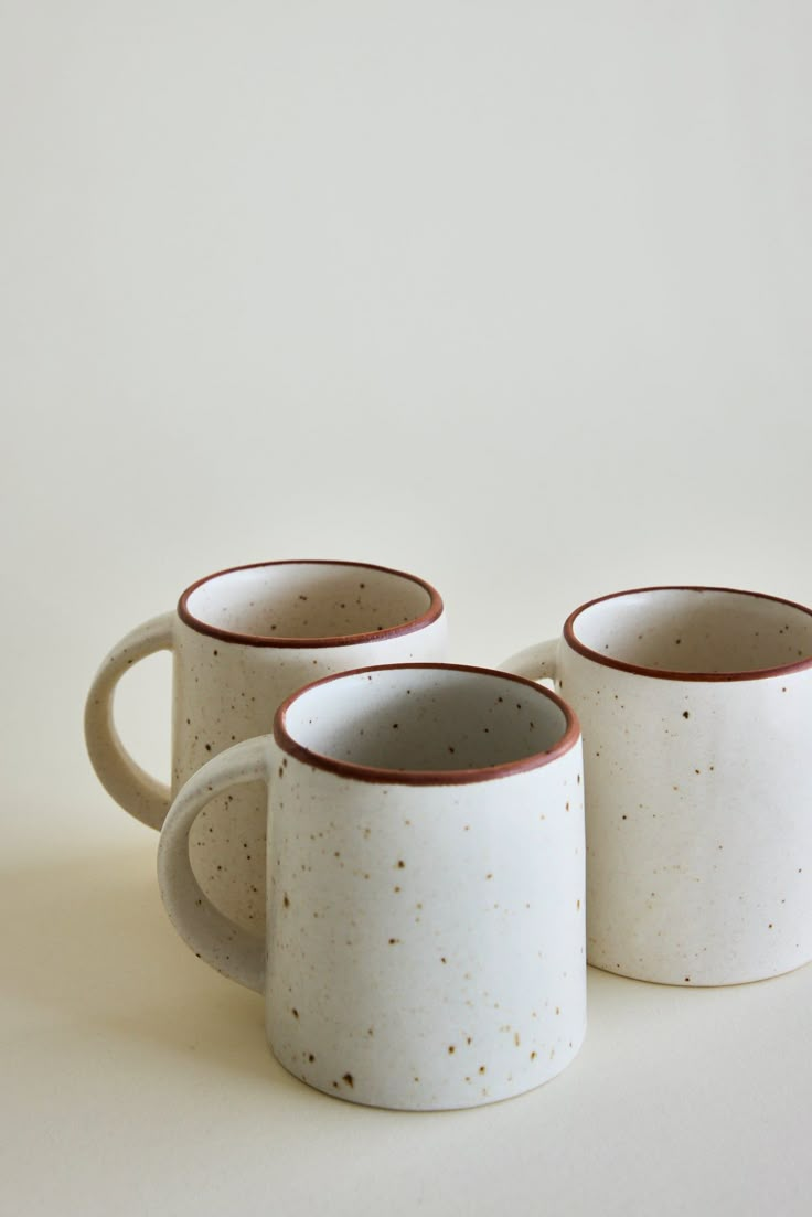 three coffee mugs sitting next to each other on a white surface with brown speckles