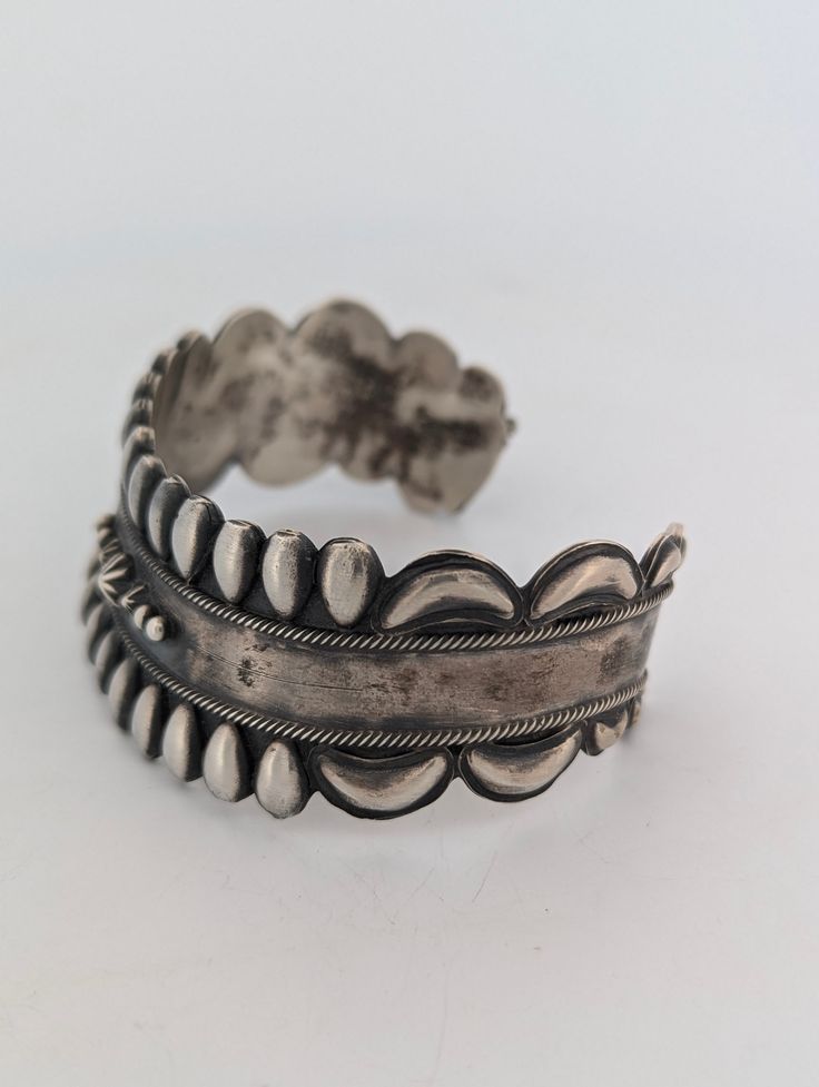 Celebrate the rich heritage of Native American craftsmanship with this vintage sterling silver cuff bracelet, a handmade treasure that exudes both strength and beauty. Stamped with a distinctive bear symbol and "RB", along with the .925 sterling silver mark, this piece is a stunning example of artistry and tradition. The repousse style design, enhanced by hand-stamped details and twisted wire accents, makes this bracelet a standout in any collection. Material: Authentic .925 sterling silver, guaranteeing high quality and durability. Design: Features a repousse style design with intricate hand-stamped details and twisted wire accents for added texture and dimension. Stamping: Bears a unique bear stamp with "RB" inside, a mark of Native American craftsmanship, alongside the .925 stamp for st Traditional Sterling Silver Bangle With Polished Finish, Antique Silver Hallmarked Bangle Jewelry, Antique Silver Hallmarked Bangle, Hallmarked Antique Silver Bangle, Classic Round Cuff Bracelet For Ceremonial Occasions, Classic Round Ceremonial Cuff Bracelet, Bohemian Sterling Silver Cuff Bracelets, Bohemian Sterling Silver Cuff Bangle, Adjustable Antique Silver Hallmarked Bracelets