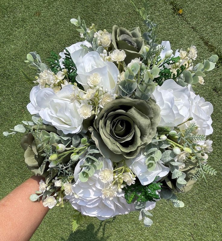 a bridal bouquet with white flowers and greenery is held by someone's hand