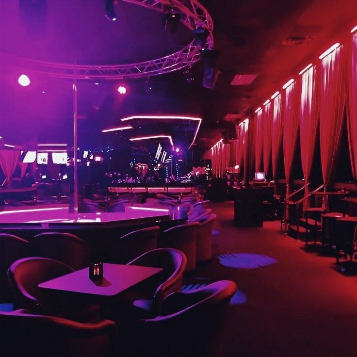 a dimly lit room with red and purple lighting on the walls, tables and chairs