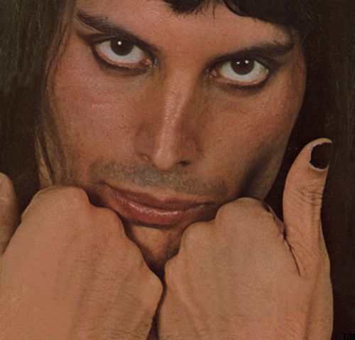 a man with long hair and blue eyes posing for the camera while holding his hands to his face