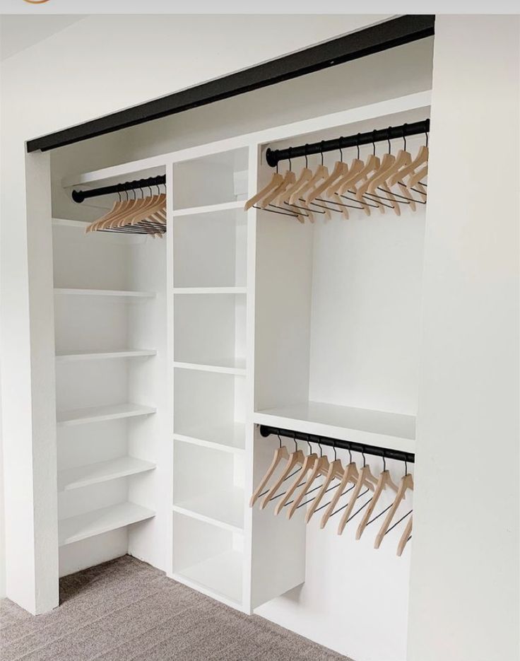 an empty closet with white shelves and wooden clothes hangers on the wall, along with carpeted flooring