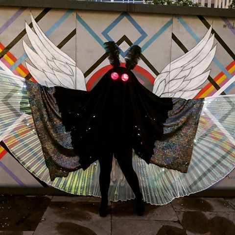 a woman standing in front of a wall with wings on it's back and red eyes