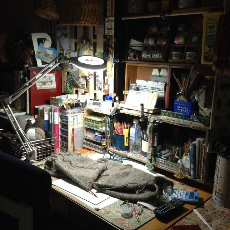 a desk with a lamp, books and other items on it in a cluttered room