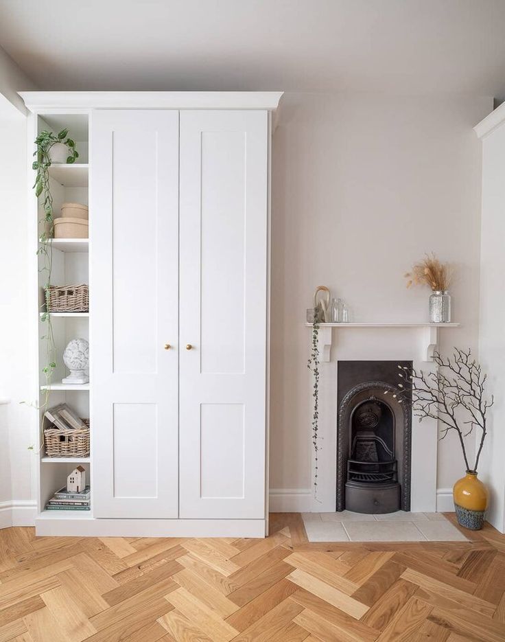 a living room with a fireplace, bookshelf and white cupboards in it