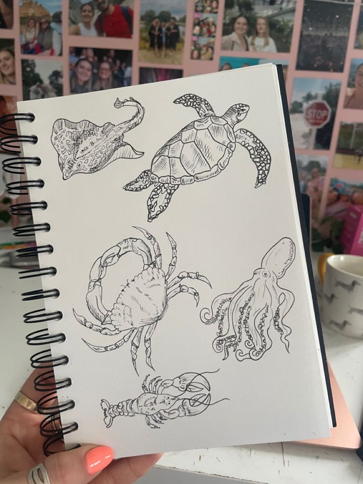 a hand holding a notebook with drawings of sea animals on it and pictures of people in the background