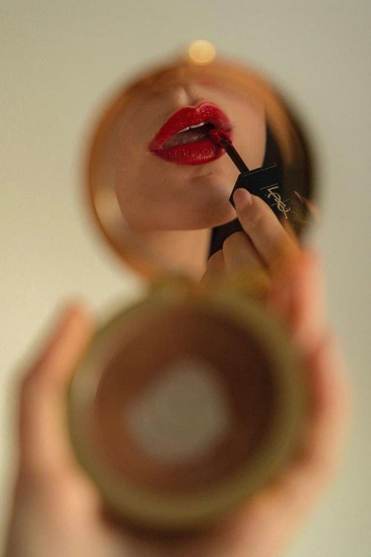 a woman holding a magnifying glass looking at her red lips in the mirror