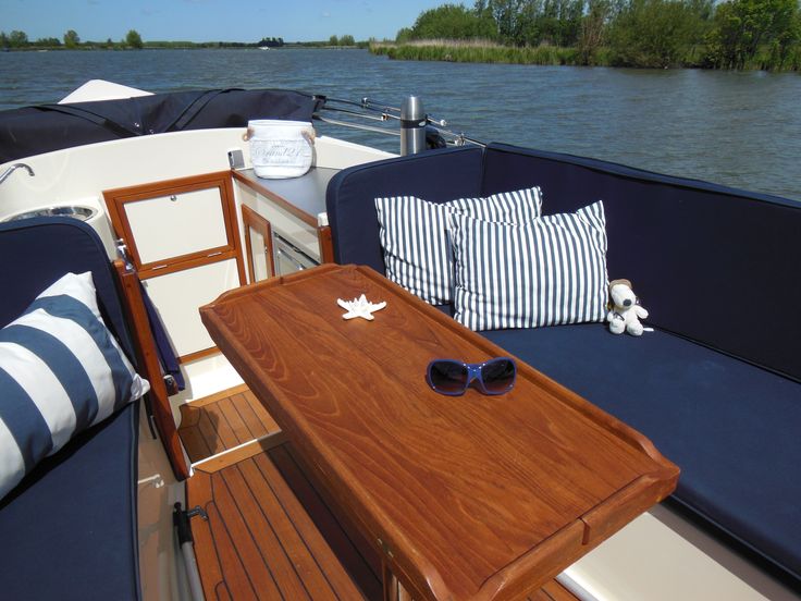 a wooden table sitting on top of a boat next to the water with two blue cushions