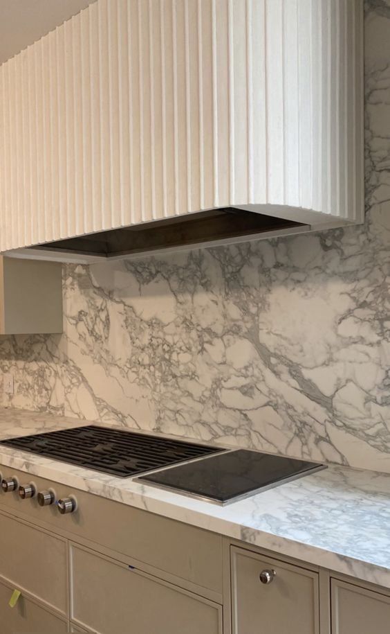 a stove top oven sitting inside of a kitchen next to white cupboards and drawers