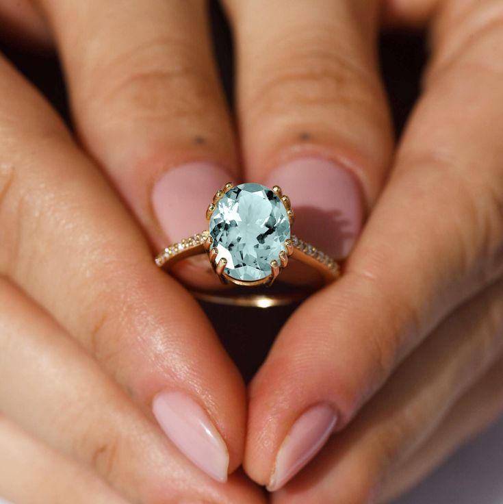 a close up of a person's hands holding a ring with a blue stone