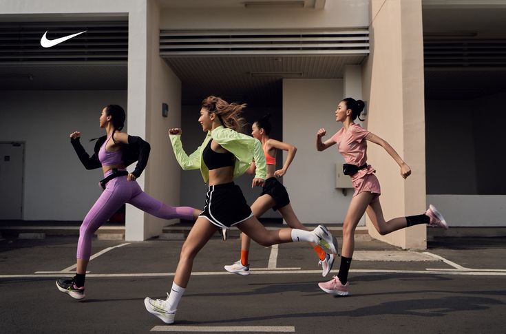 a group of women running across a parking lot in front of a white nike building