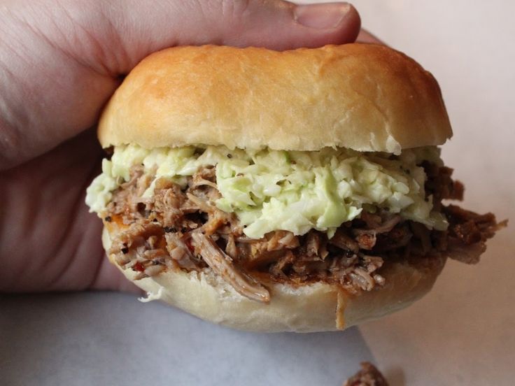 a hand holding a pulled pork sandwich with cole slaw on it's bun