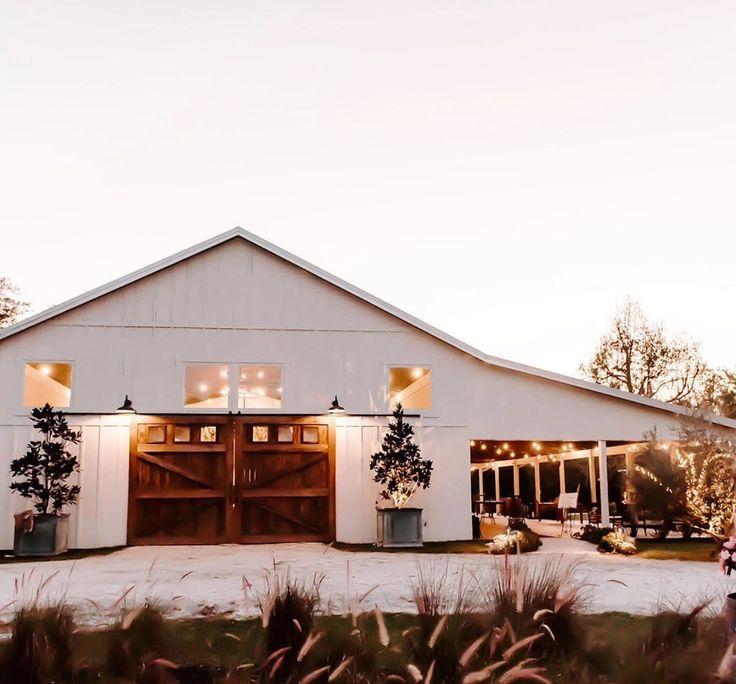 a large white barn with lights on it's doors and windows in the front